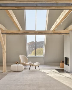 Design Lounge-Sessel mit passendem Hocker in hellem Stoff, moderne Wohnraumgestaltung mit Dachfenster und Kamin – hochwertige Designer-Sitzmöbel für exklusive Wohnkonzepte in Trier, Konz und Luxemburg